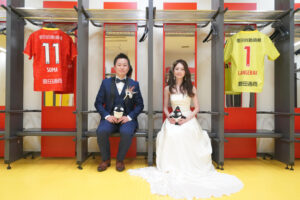 豊田スタジアムでウェディングドレス前撮り　グランパスのロッカールームでグランパスくんを持つふたり