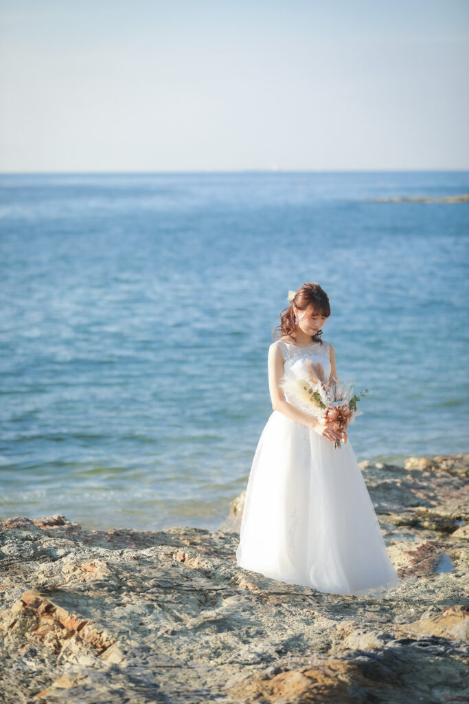 海をバックにブーケを見つめるウェディングドレスを着た花嫁