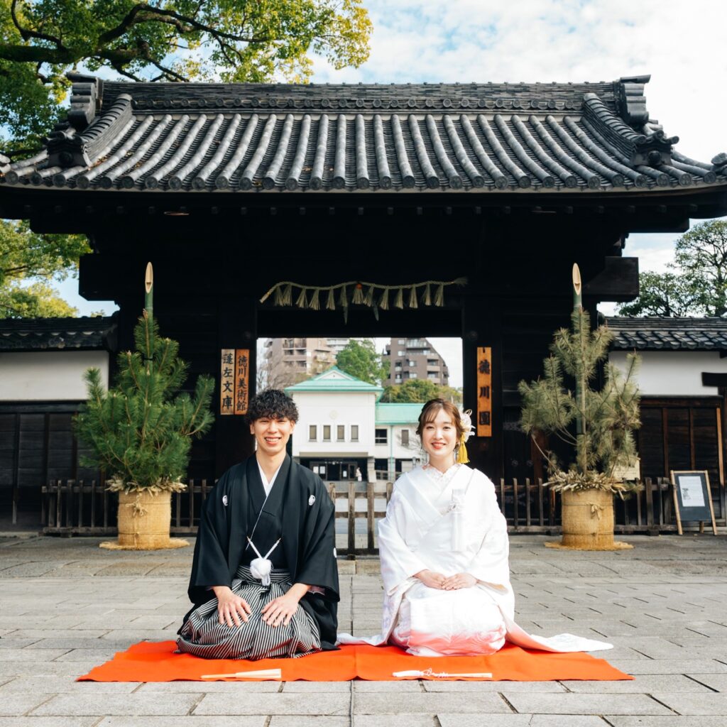 徳川園の正門の前で正座をする紋付き袴姿の新郎と白無垢姿の新婦