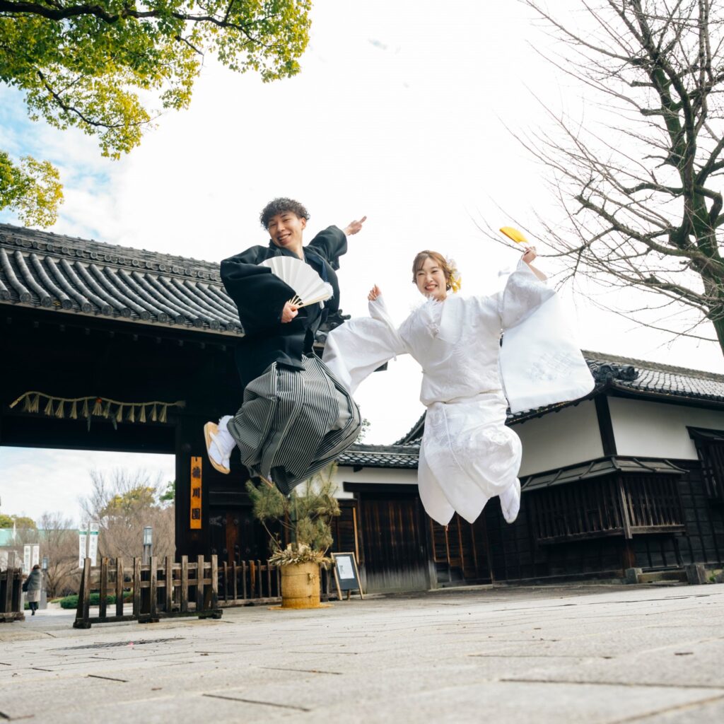 徳川園の正門前でポーズを決めてジャンプする和装姿の新郎新婦