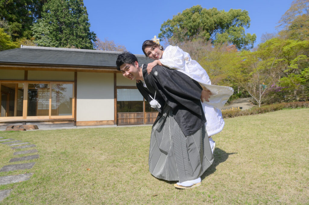 東山植物園内で紋付き袴姿の新郎が白無垢姿の新婦をおんぶする