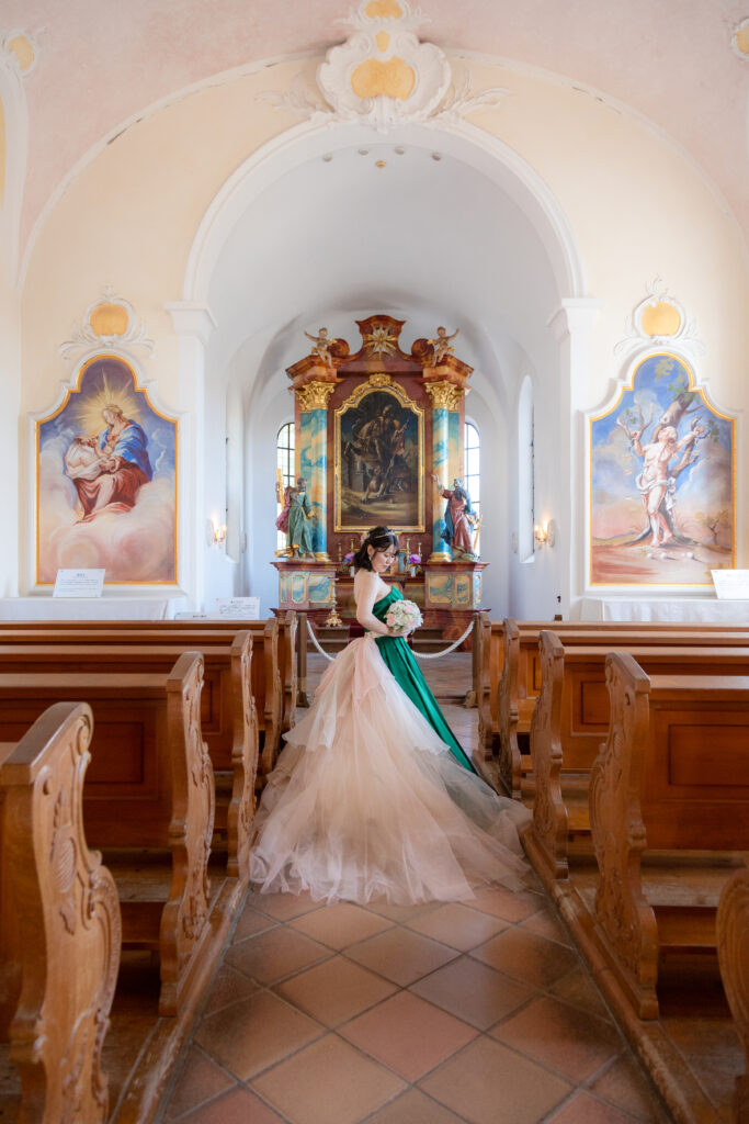 リトルワールド内のチャペルでブーケを見つめるグリーンのドレスを着た花嫁
