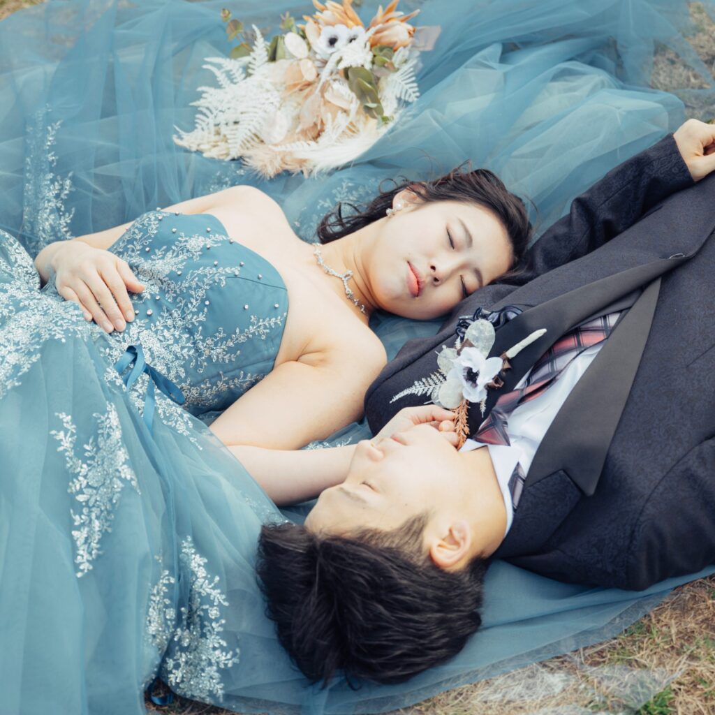 庄内緑地公園の芝生の上に寝転がるタキシード姿の新郎とカラードレス姿の新婦