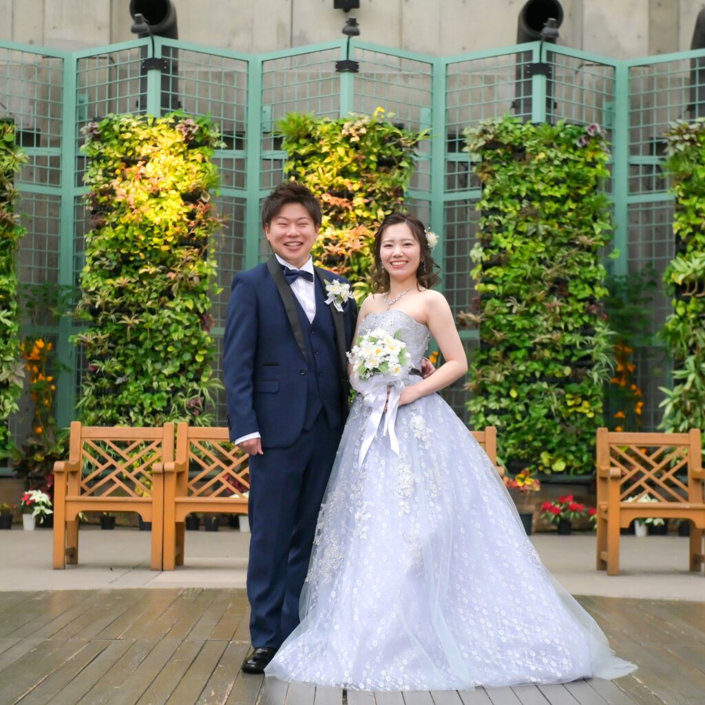 フラリエにあるお花の前で微笑むタキシード姿の新郎とドレス姿の新婦