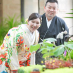 フラリエで和装前撮り 赤以外の色打掛を着て花を見てほほ笑む新郎新婦